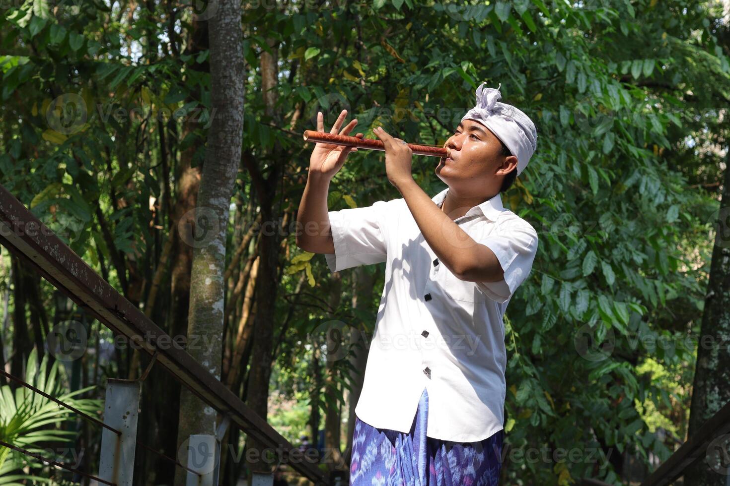 Portrait of Asian man wearing balinese traditional cloth playing bamboo flute in outdoor park photo