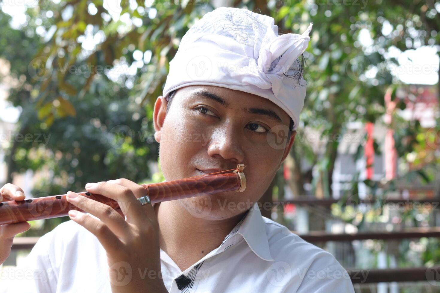 Portrait of Asian man wearing balinese traditional cloth playing bamboo flute in outdoor park photo
