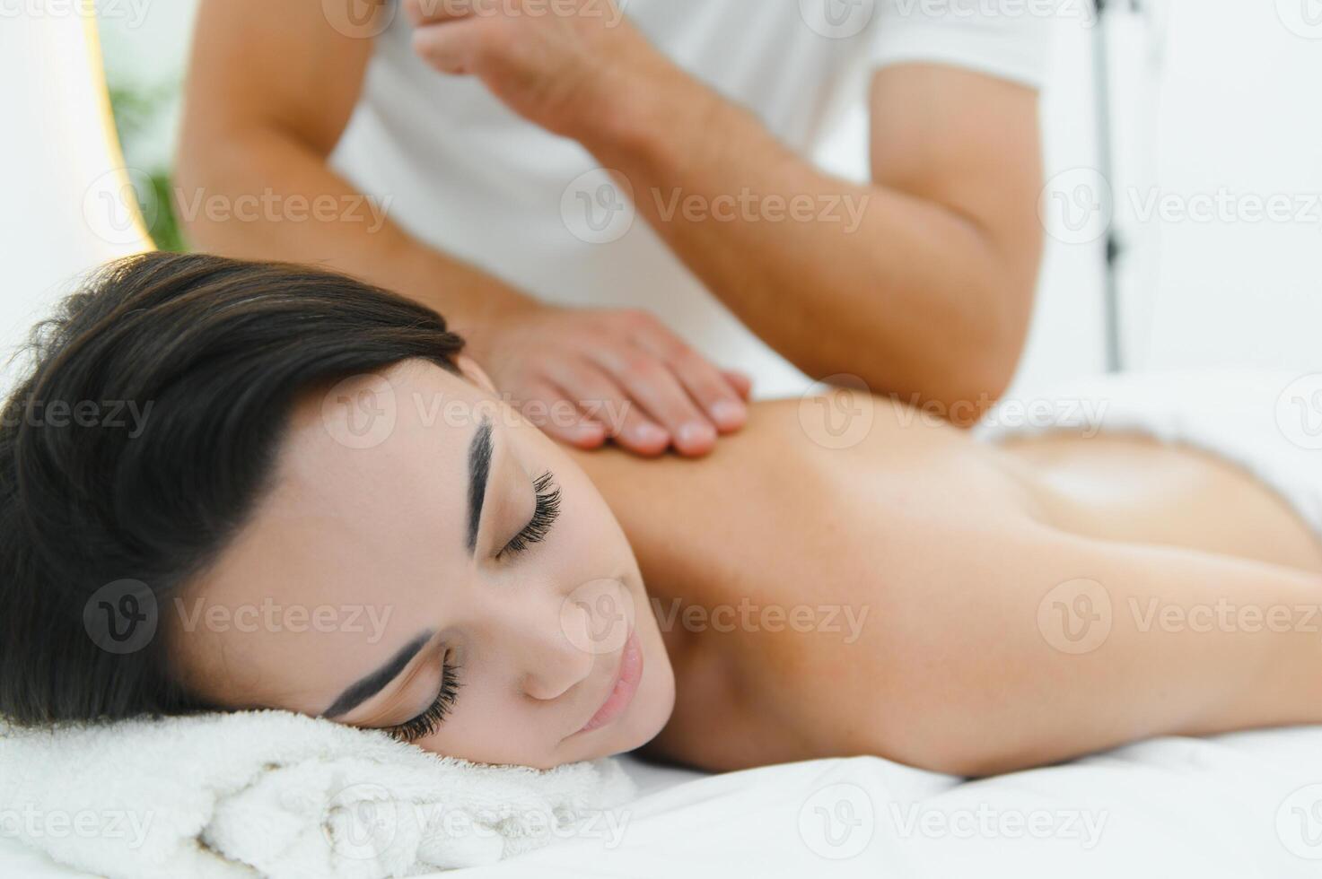 A young brunette woman receives a professional back massage in a spa salon. A beautiful naked lady in a towel with perfect skin gets a relaxing massage. The concept of luxury professional massage photo
