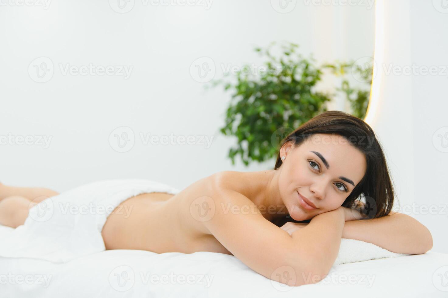 Portrait of satisfied carefree woman lying on massage table enjoying leisure in beauty parlor. Happy relaxed beautiful female having rest at luxury photo