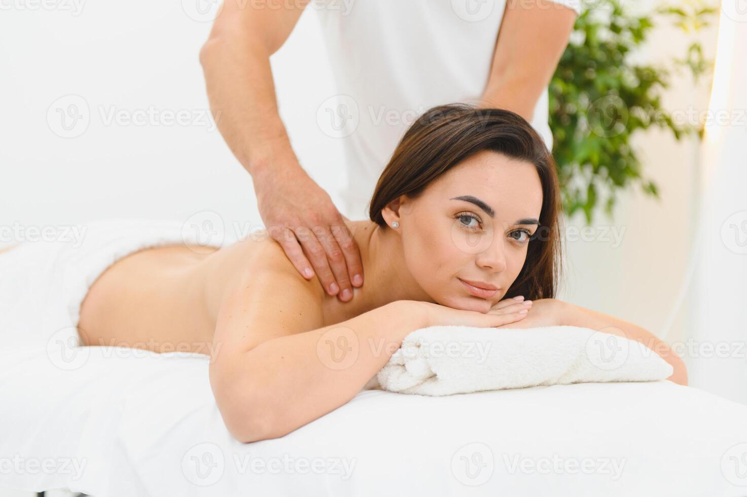 A young brunette woman receives a professional back massage in a spa salon. A beautiful naked lady in a towel with perfect skin gets a relaxing massage. The concept of luxury professional massage photo