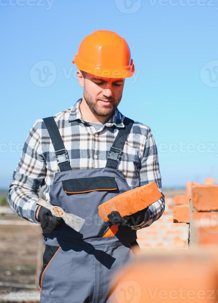 Male construction worker in uniform and helmet on construction of red brick house photo
