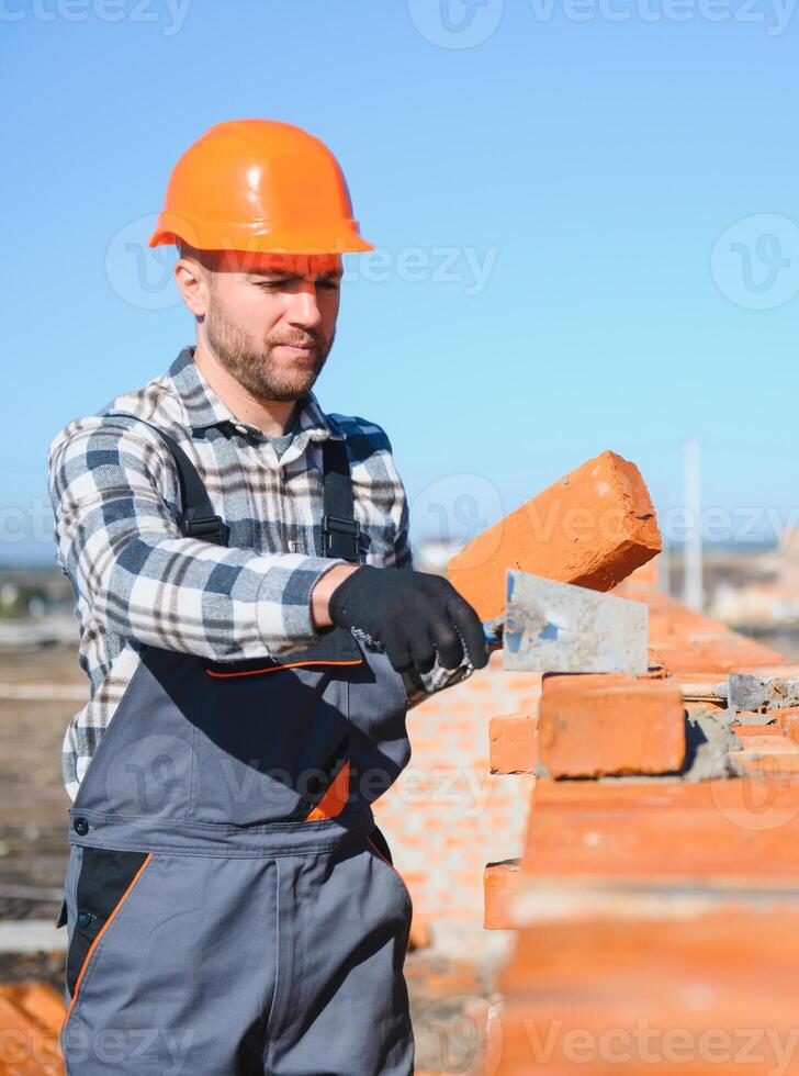 Bricklayer industrial worker installing brick masonry on exterior wall with trowel putty knife photo