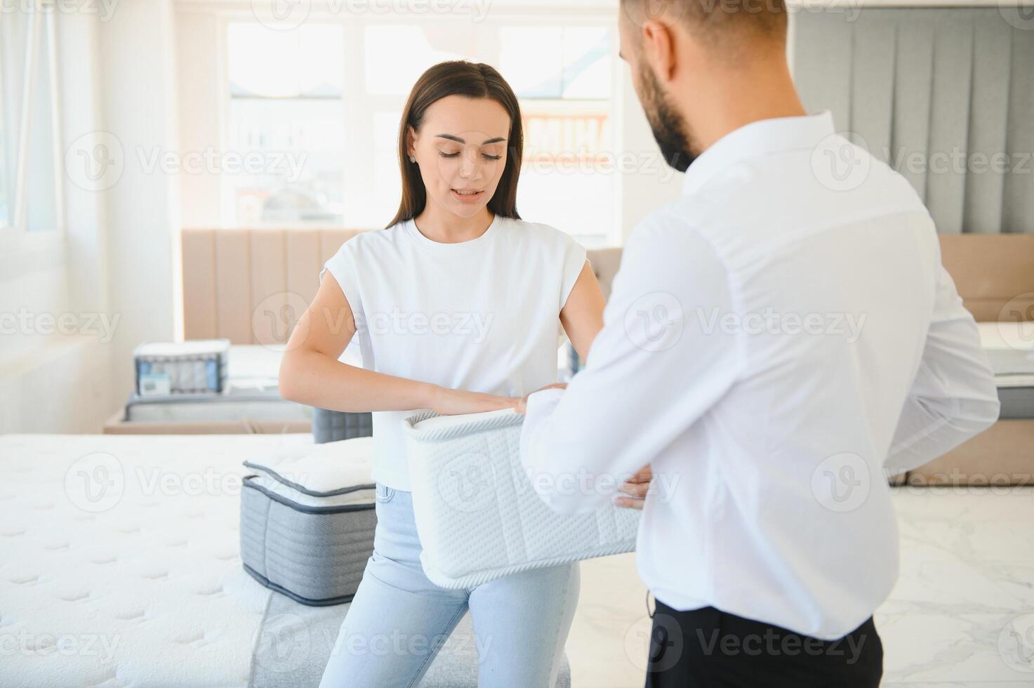 A young seller in a furniture store showing samples of mattresses in a bed photo