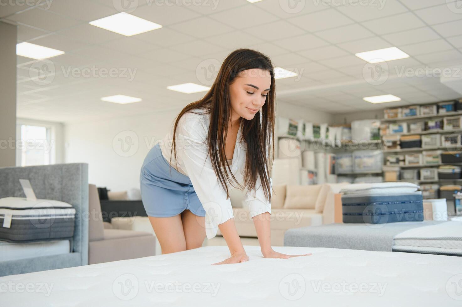 A woman in a white shirt in a mattress store. She examines the mattress she wants to buy photo
