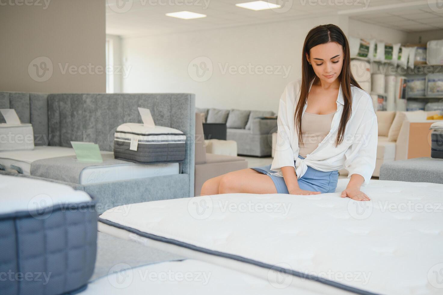 happy brunette female is sitting on mattress for testing it in the store photo