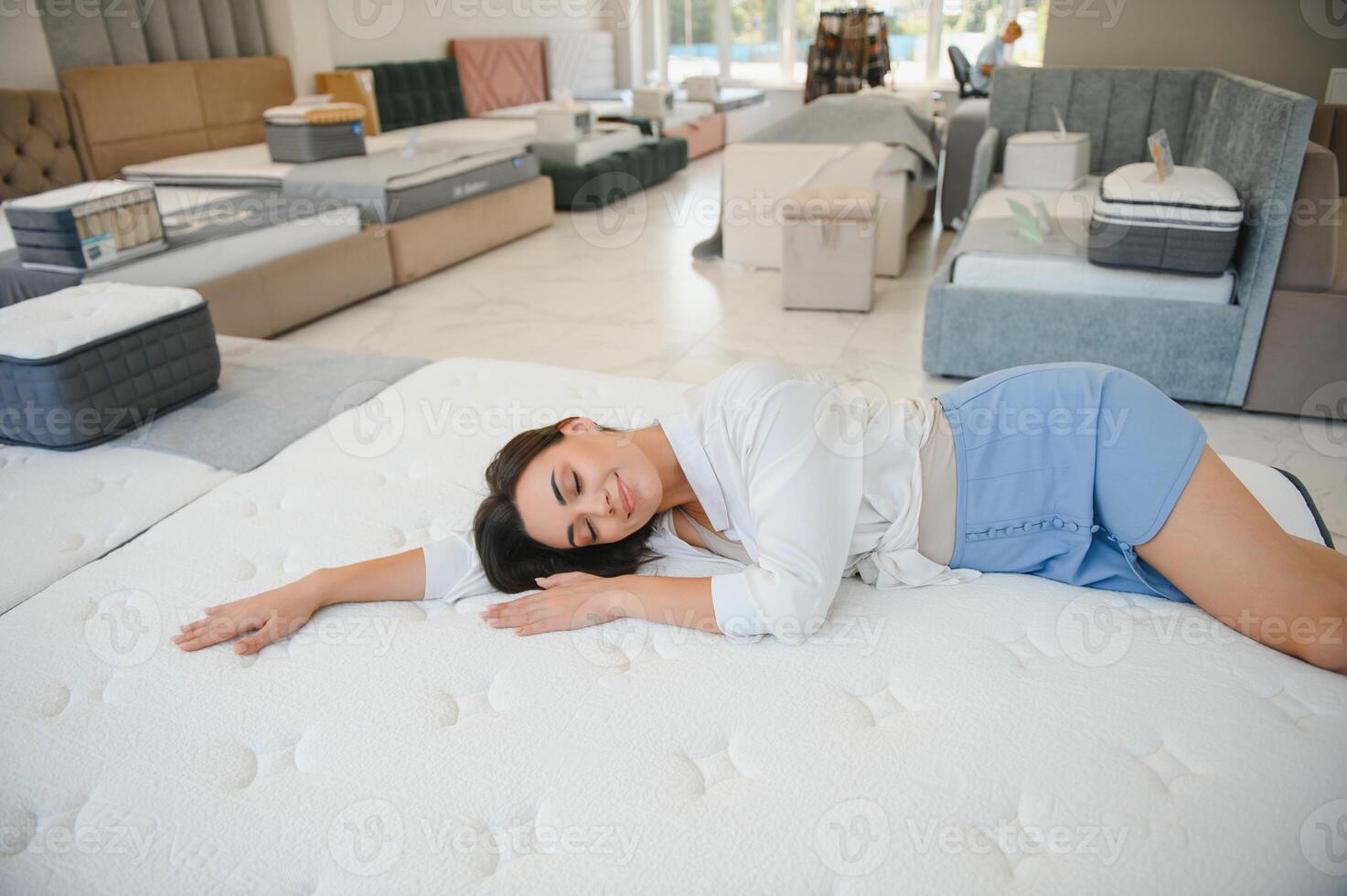 happy brunette female is sitting on mattress for testing it in the store photo