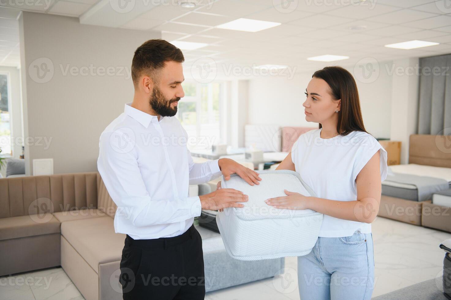 A young seller in a furniture store showing samples of mattresses in a bed photo