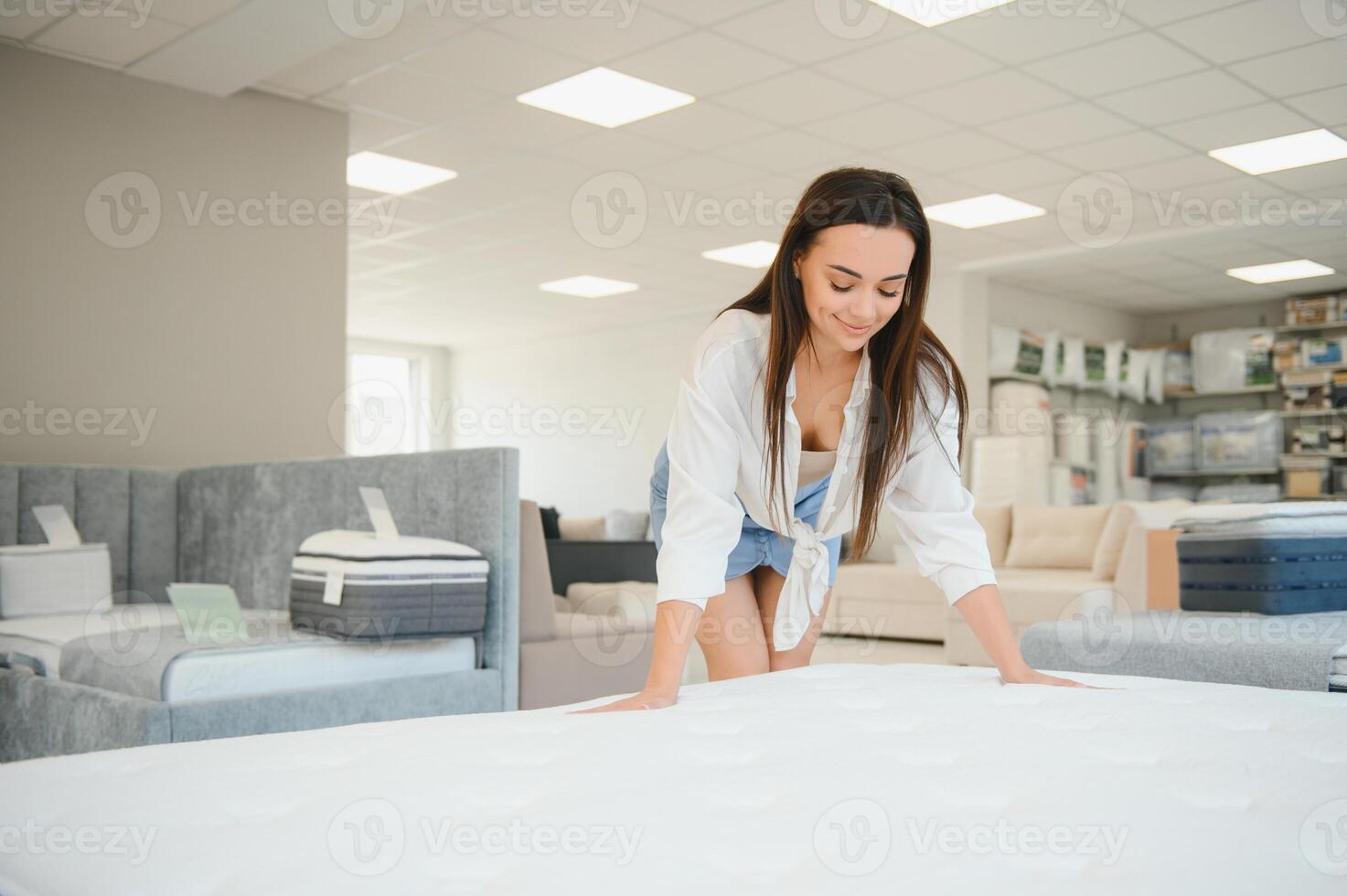 A woman in a white shirt in a mattress store. She examines the mattress she wants to buy photo