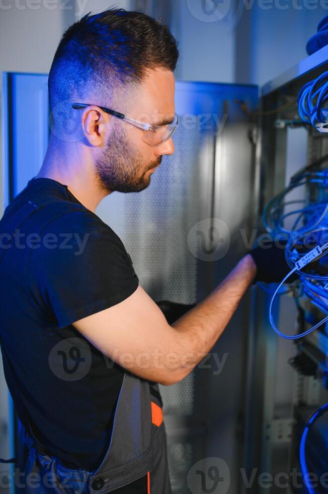 Young man is working with internet equipment and wires in server room photo
