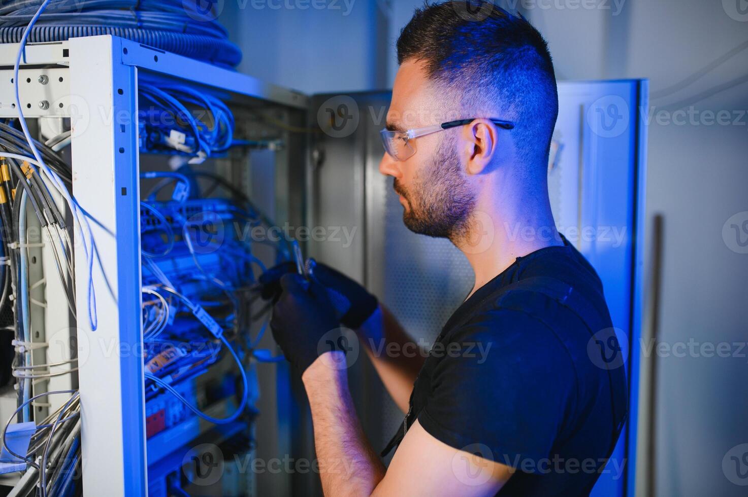 Young man is working with internet equipment and wires in server room photo