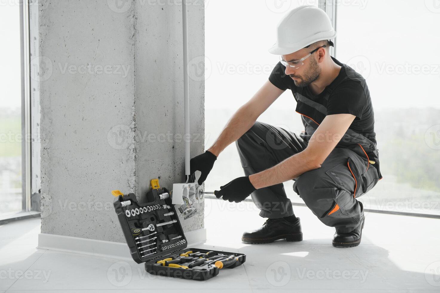 Confident professional electrician in uniform using screwdriver while replacing a socket in apartment after renovation work photo