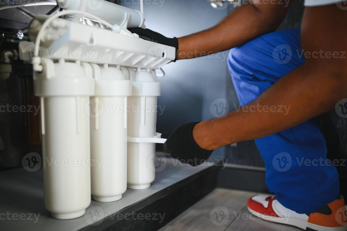 Plumber installs or change water filter. Replacement aqua filter. Repairman installing water filter cartridges in a kitchen photo