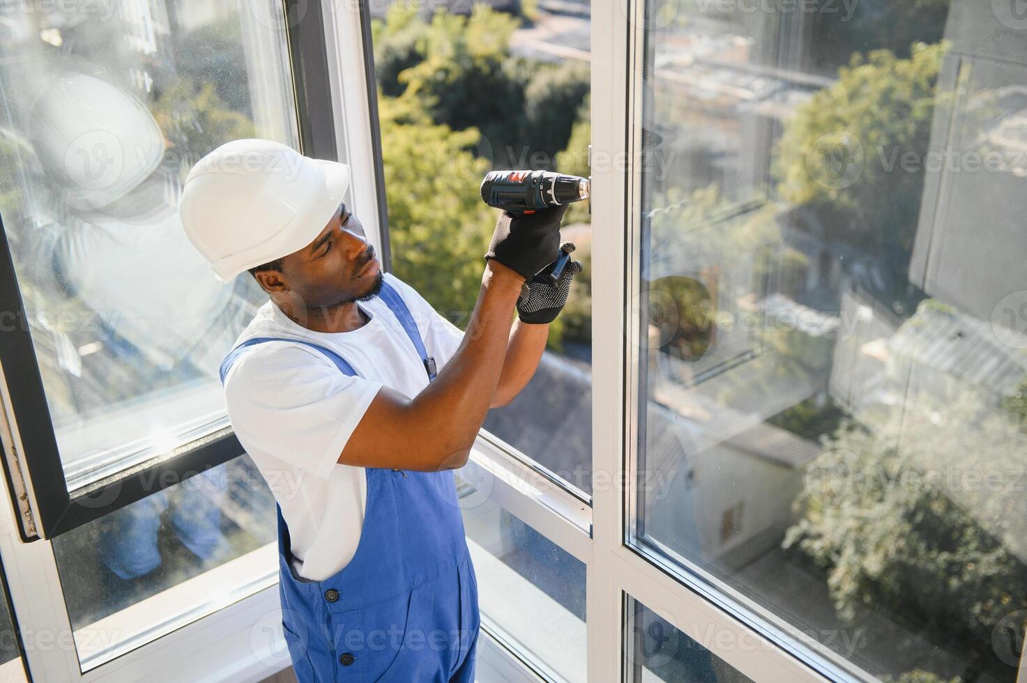 African Workman in overalls installing or adjusting plastic windows in the living room at home photo