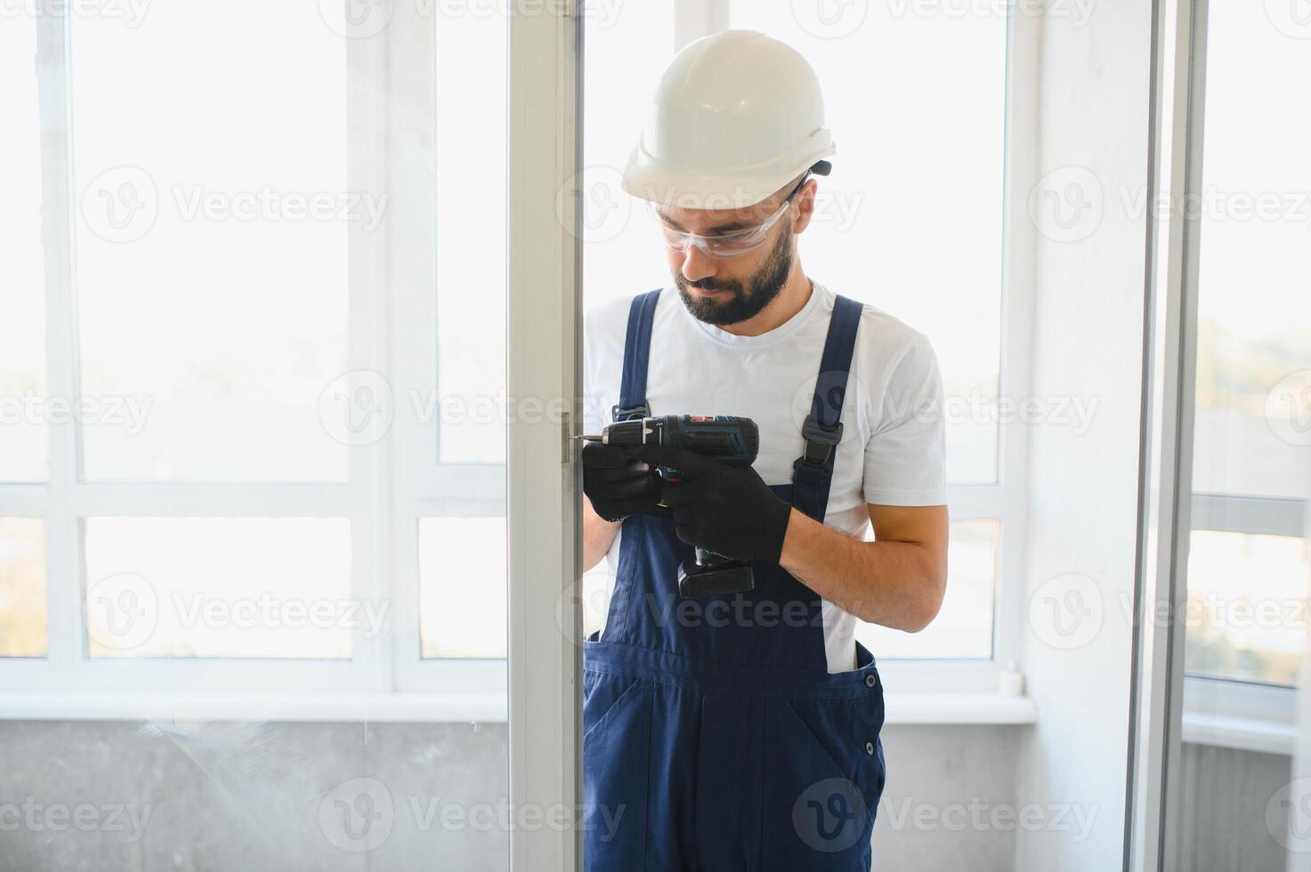 Workman in overalls installing or adjusting plastic windows in the living room at home photo