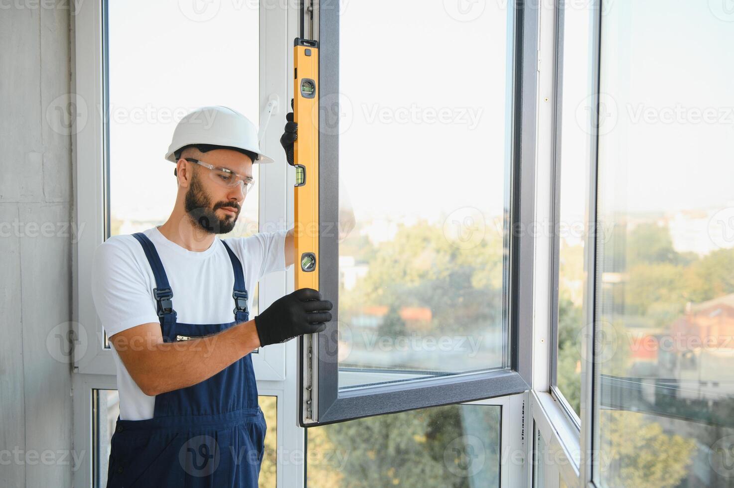 Workman in overalls installing or adjusting plastic windows in the living room at home photo