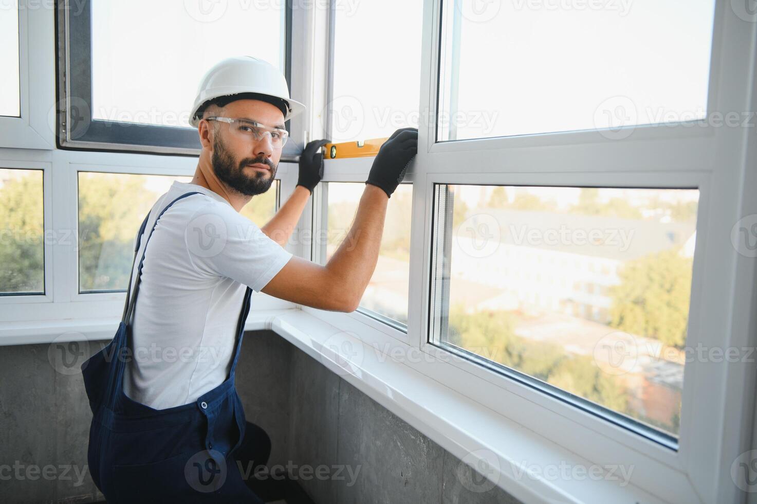 Workman in overalls installing or adjusting plastic windows in the living room at home photo