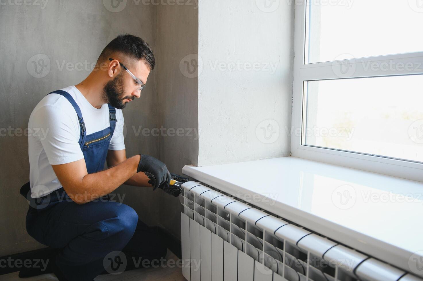 A plumber is fixing a radiator. With an adjustable wrench, he tightens the tap photo