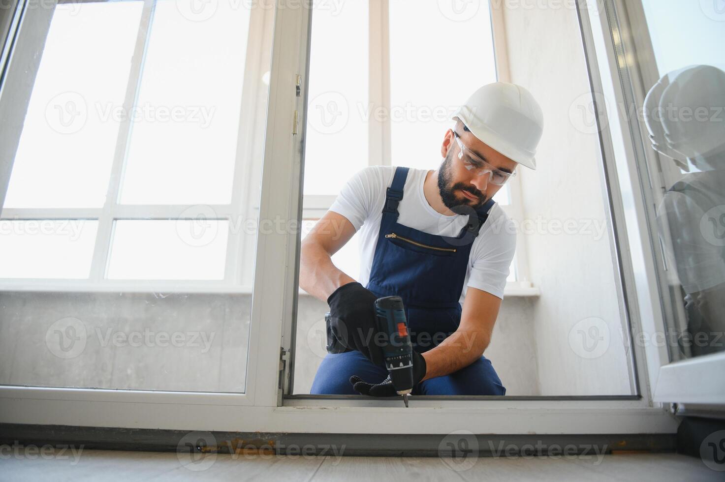 Workman in overalls installing or adjusting plastic windows in the living room at home photo