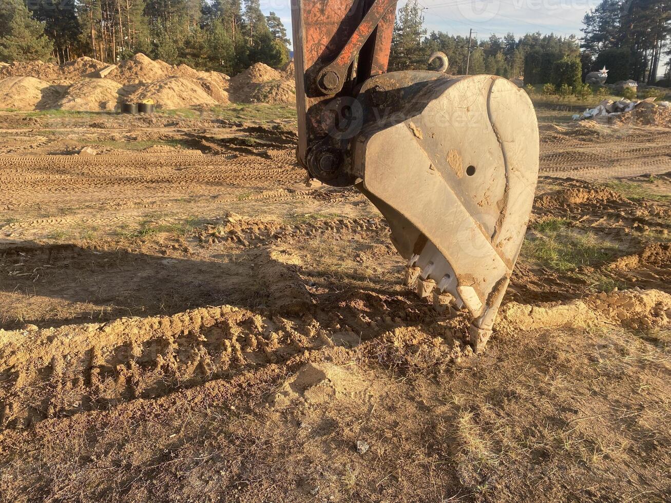 Excavator bucket digs dry sandy soil at a construction site photo