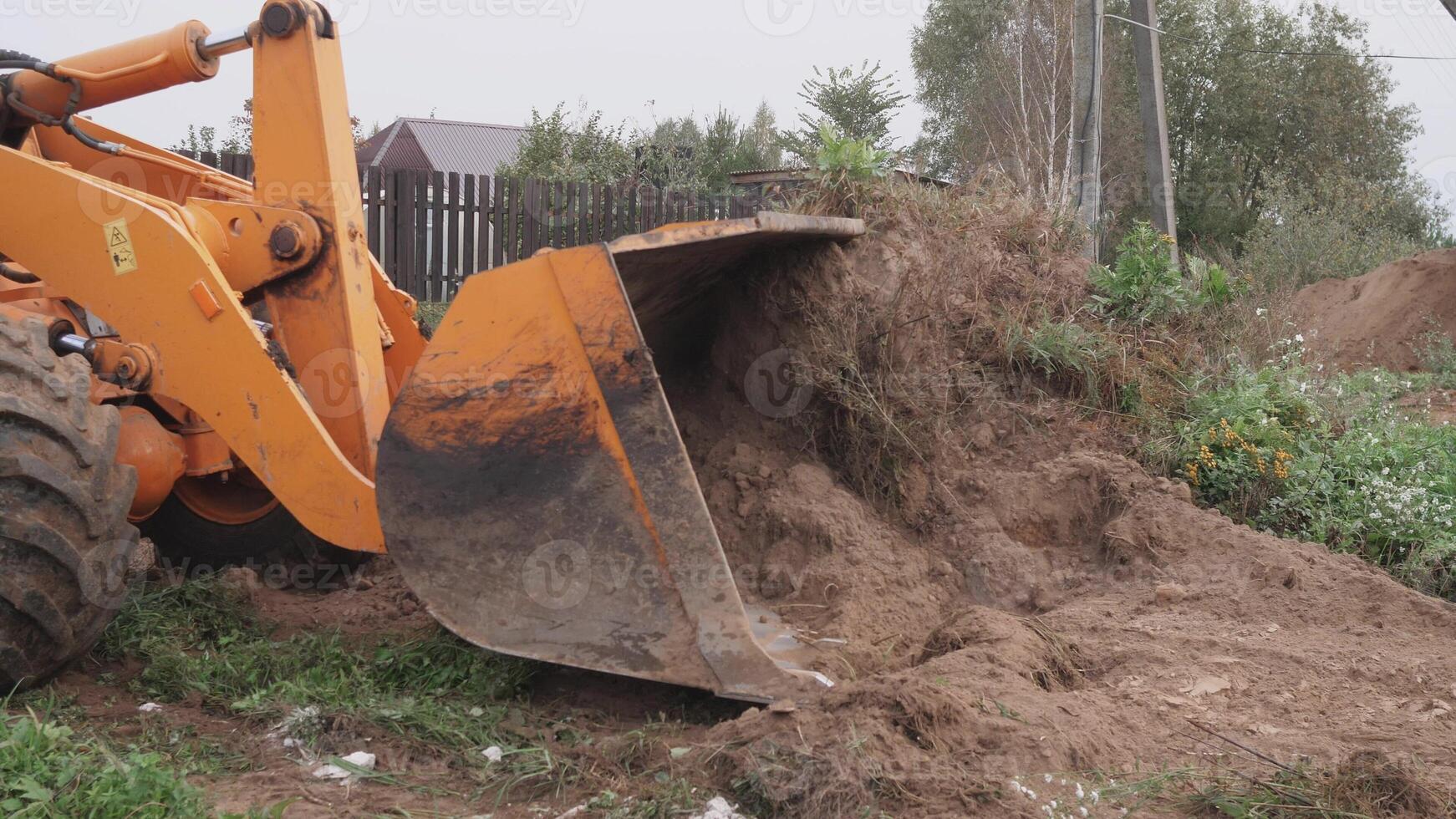 An excavator bucket is actively lifting dirt at a construction site which is surrounded by lush greenery photo