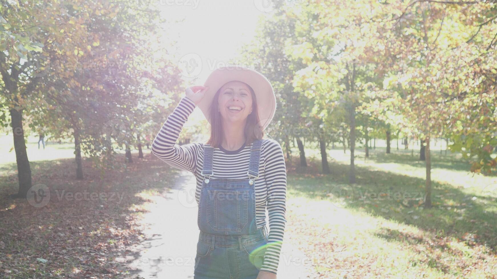 A cheerful woman wearing a stylish hat happily enjoys a sunny day surrounded by vibrant autumnal trees photo