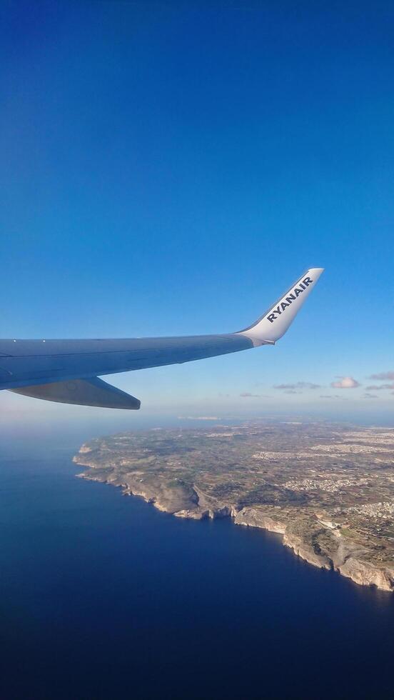 Luqa, Malta 9.01.2020. Ryanair airplane wing soaring over picturesque Maltese coastline cliff, showcasing deep blue sea and clear sky during flight. photo
