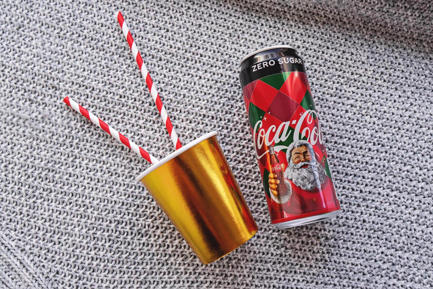 Tallinn, Estonia -30.11.2019 - Holiday-themed drink Coca Cola can with golden paper cup with red and white striped straws on gray photo