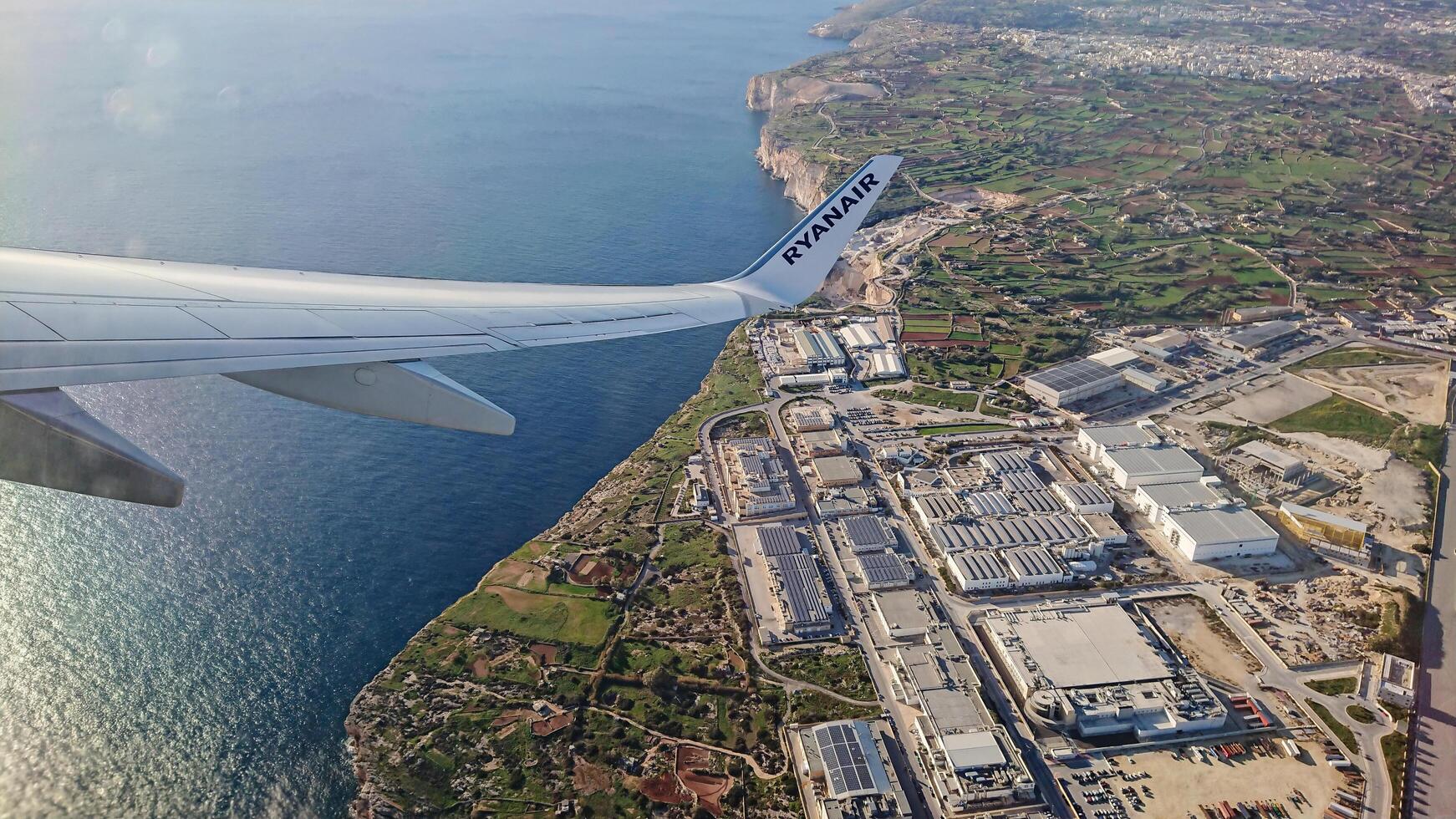 Luqa, Malta 9.01.2020. Aerial view from Ryanair airplane wing showing coastal landscape of Malta with blue sea and an industrial zone during flight photo