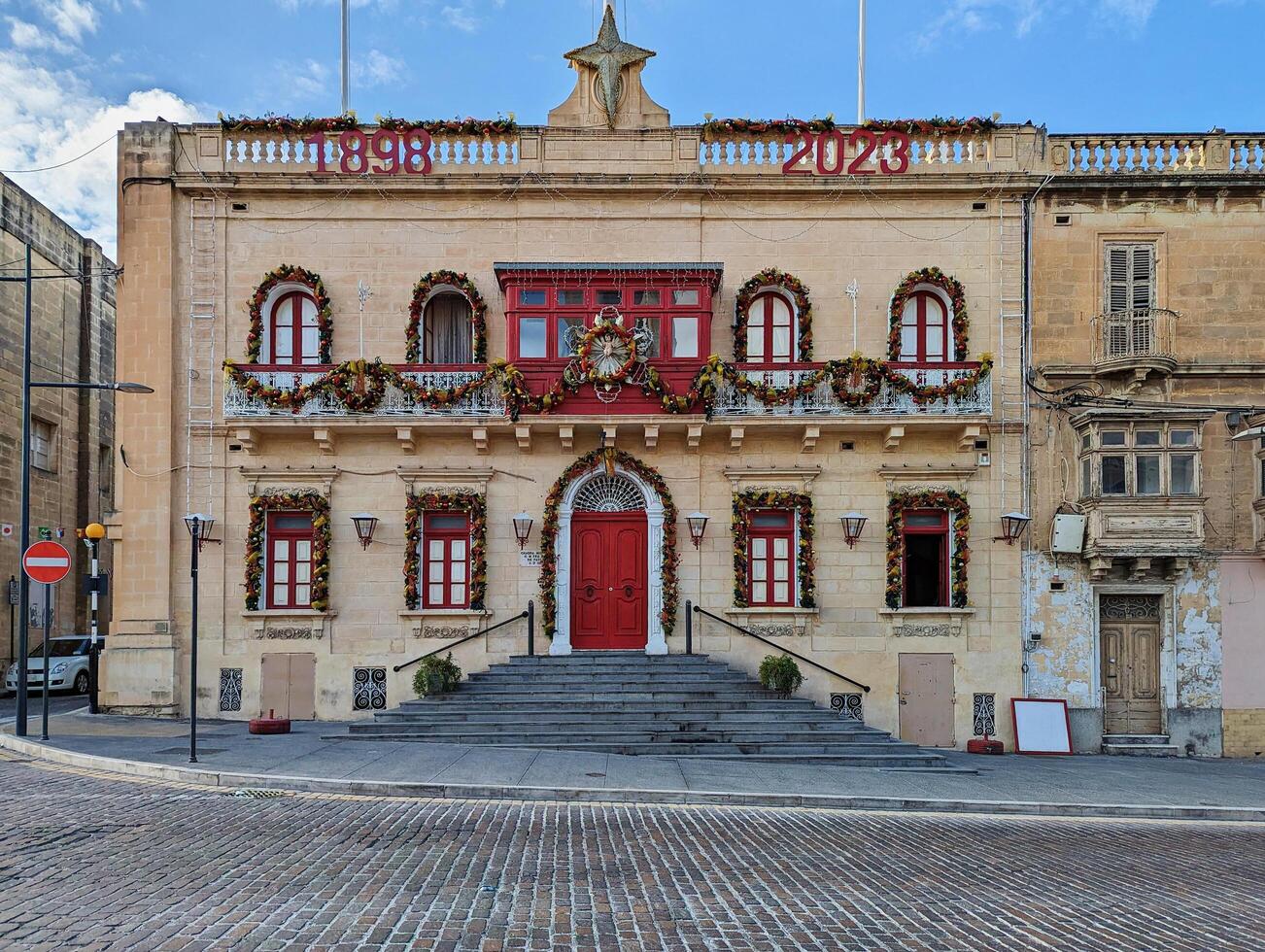 Paola, Malta,16.12.2024 - Historic Maltese Building Decorated for Christmas with Festive Garlands and Red Accents photo