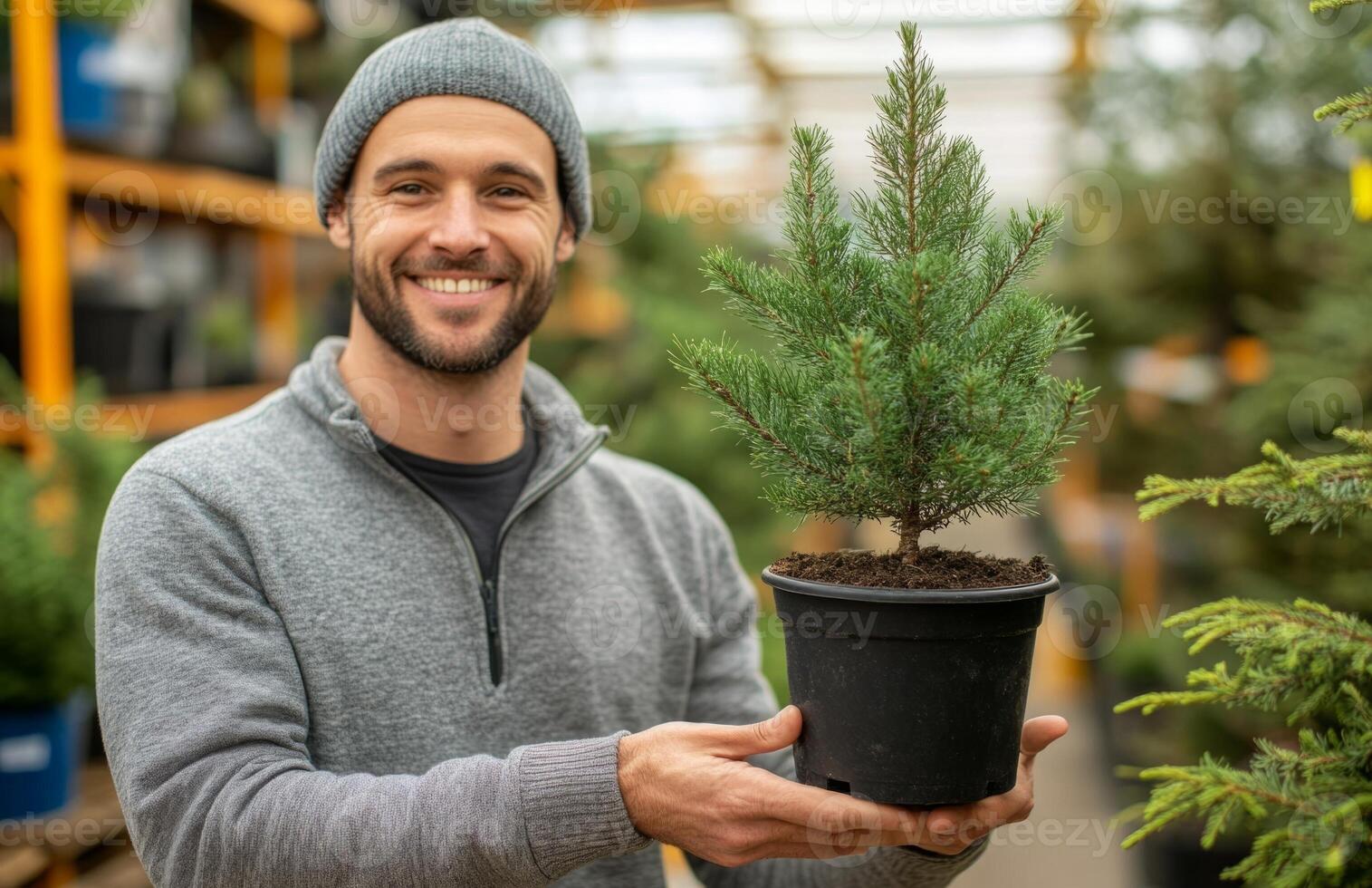 A smiling man holding a small tree in a pot photo