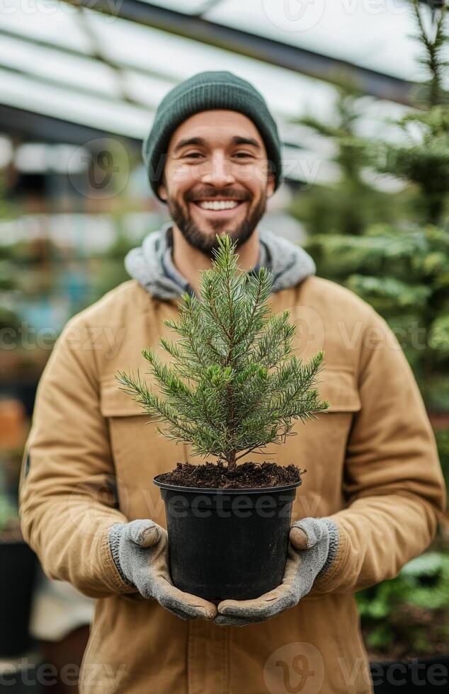 A smiling man holding a small tree in a pot photo