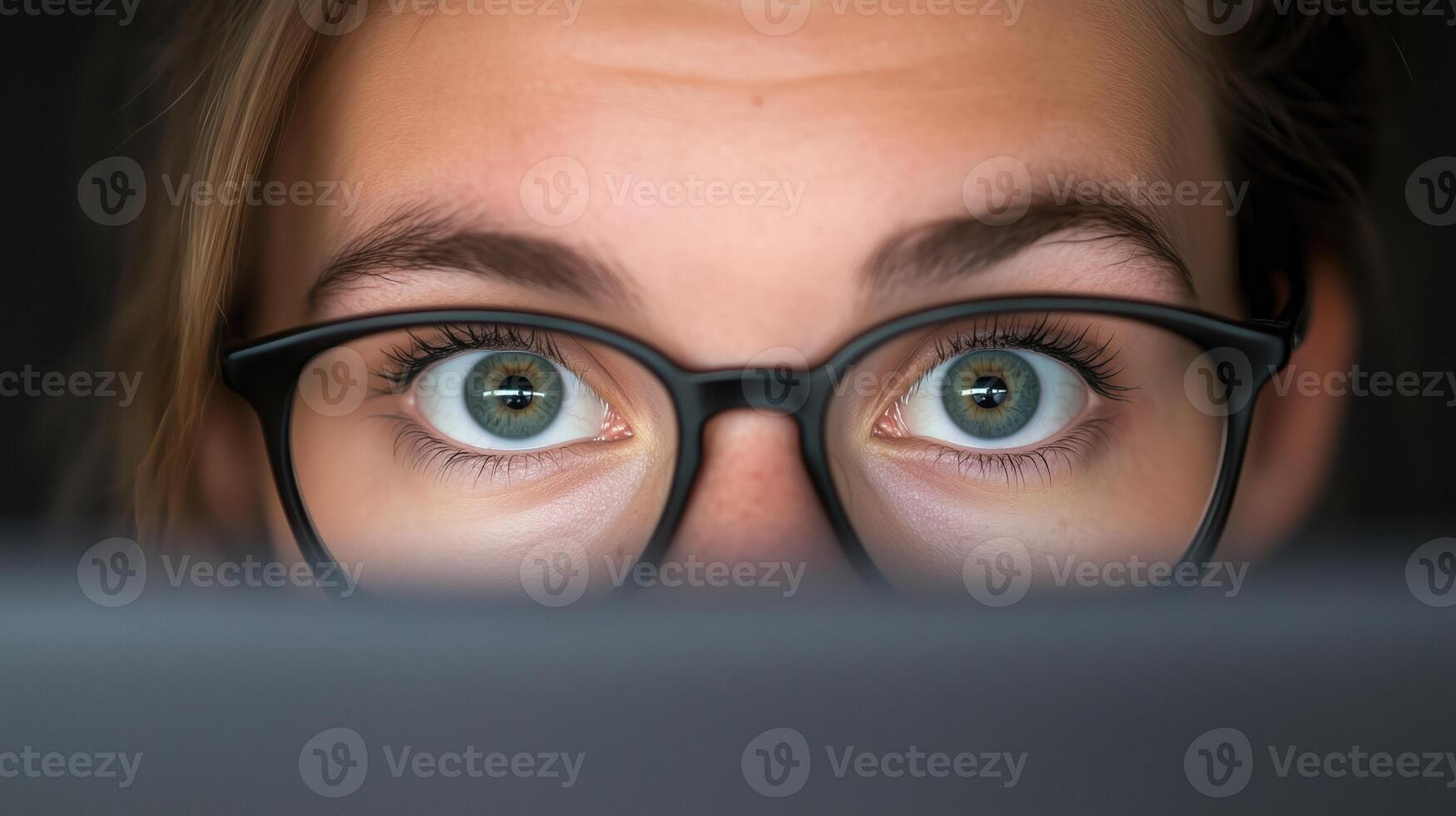 Woman With Glasses Focused on Computer Screen in Dark Room Capturing Modern Technology and Intense Concentration. Emphasizing Eyewear Style, Digital Work Environment, and Eye Expression photo