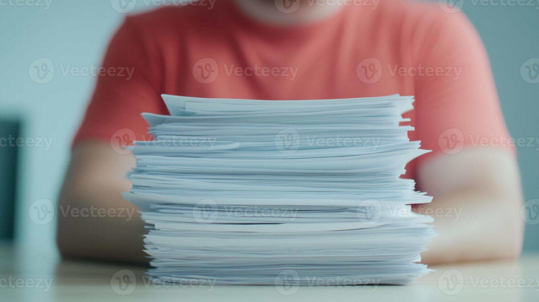 Stack Of Documents And Reports On Desk With Person In Background Wearing Red Shirt Showing Office Workload And Organization photo