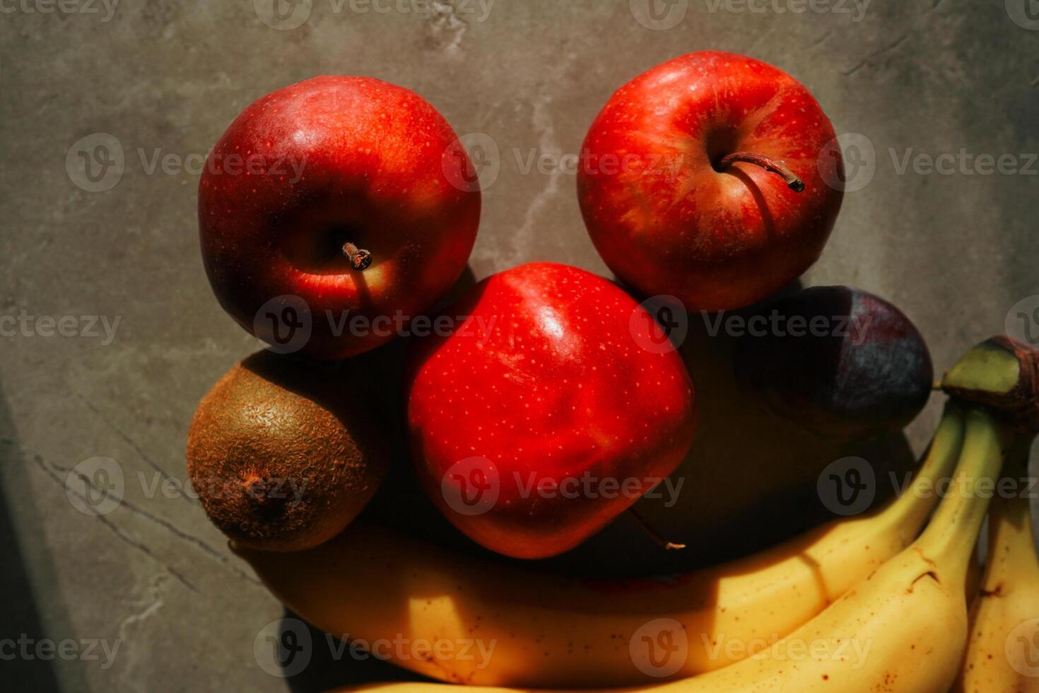 A fruit on grey background including bananas,apples, and kiwi on a countertop. photo