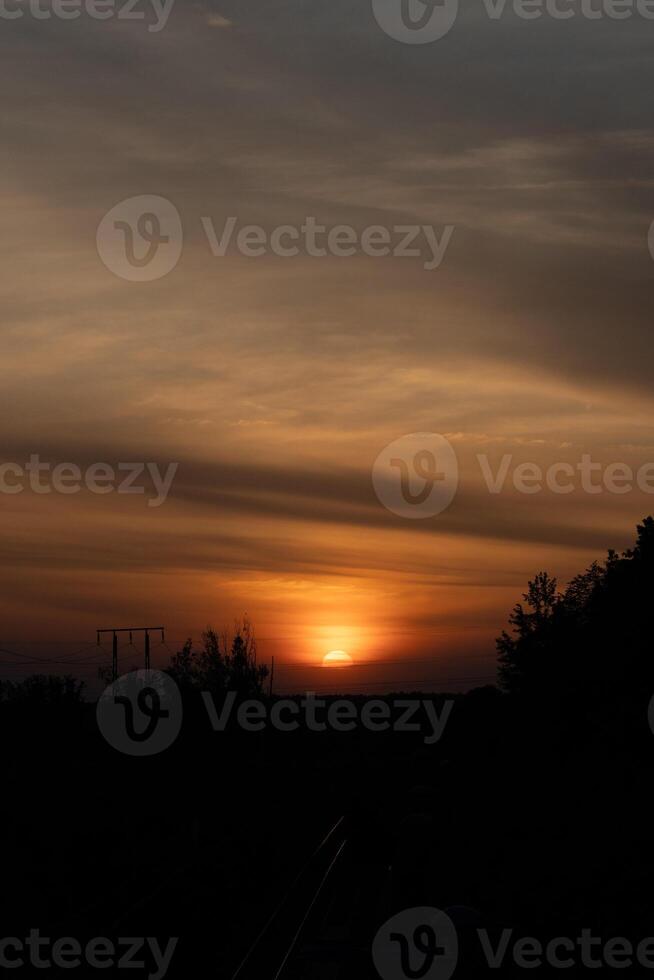 A stunning sunset with the large, radiant sun halfway below the horizon, casting a warm golden glow across the sky and railway. and the sky is adorned with subtle cloud photo