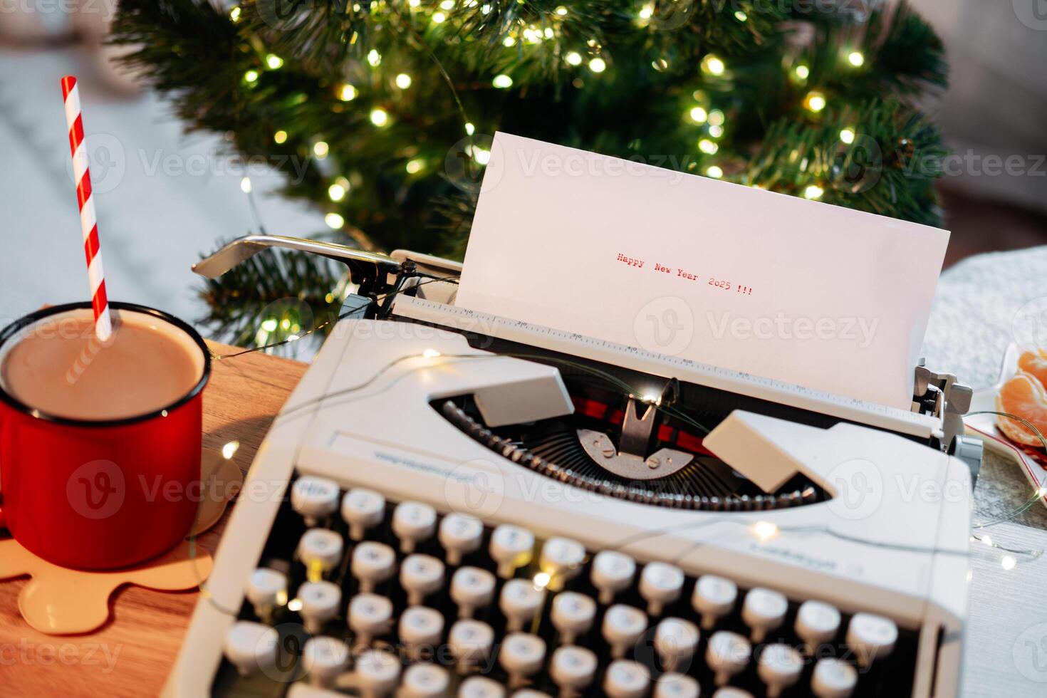 Typed on a typewriter- Happy New Year 2025, against the backdrop of a Christmas tree with garland and cocoa with tangerines on a wooden tray photo