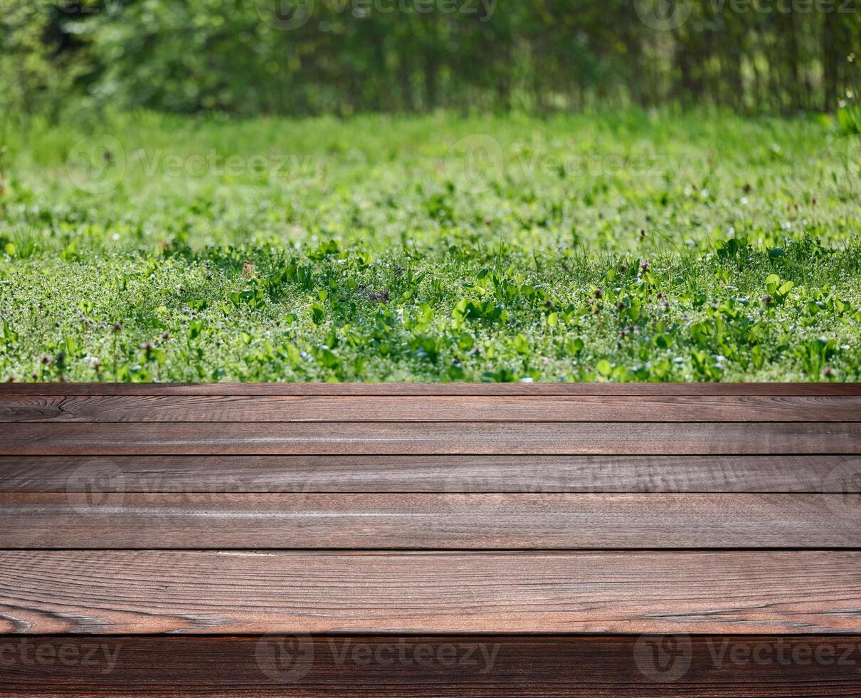Empty brown wooden table made of old gray pine boards on the background of a lawn with green juicy grass photo