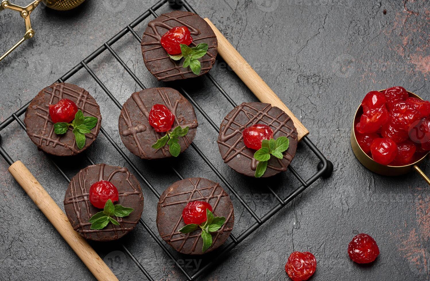 Deliciously rich chocolate brownies garnished with vibrant cherries and mint leaves, resting on a black wire rack. photo