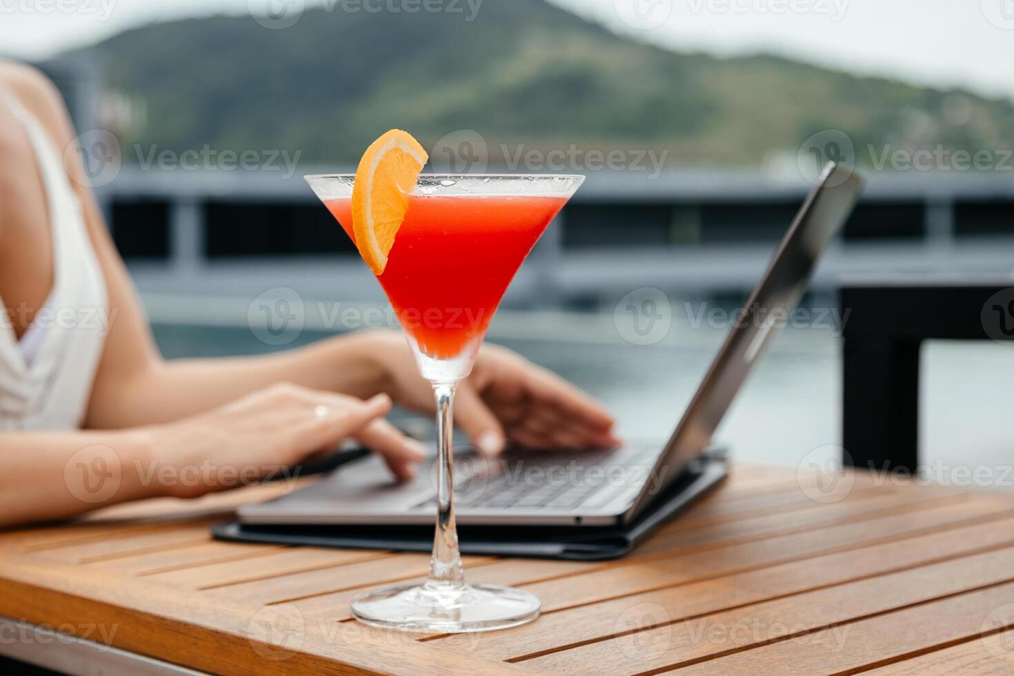 Laptop and glass of refreshing red cocktail on a table background. Work and travel or remote business concept.. Out of office work concept. Free copy space photo