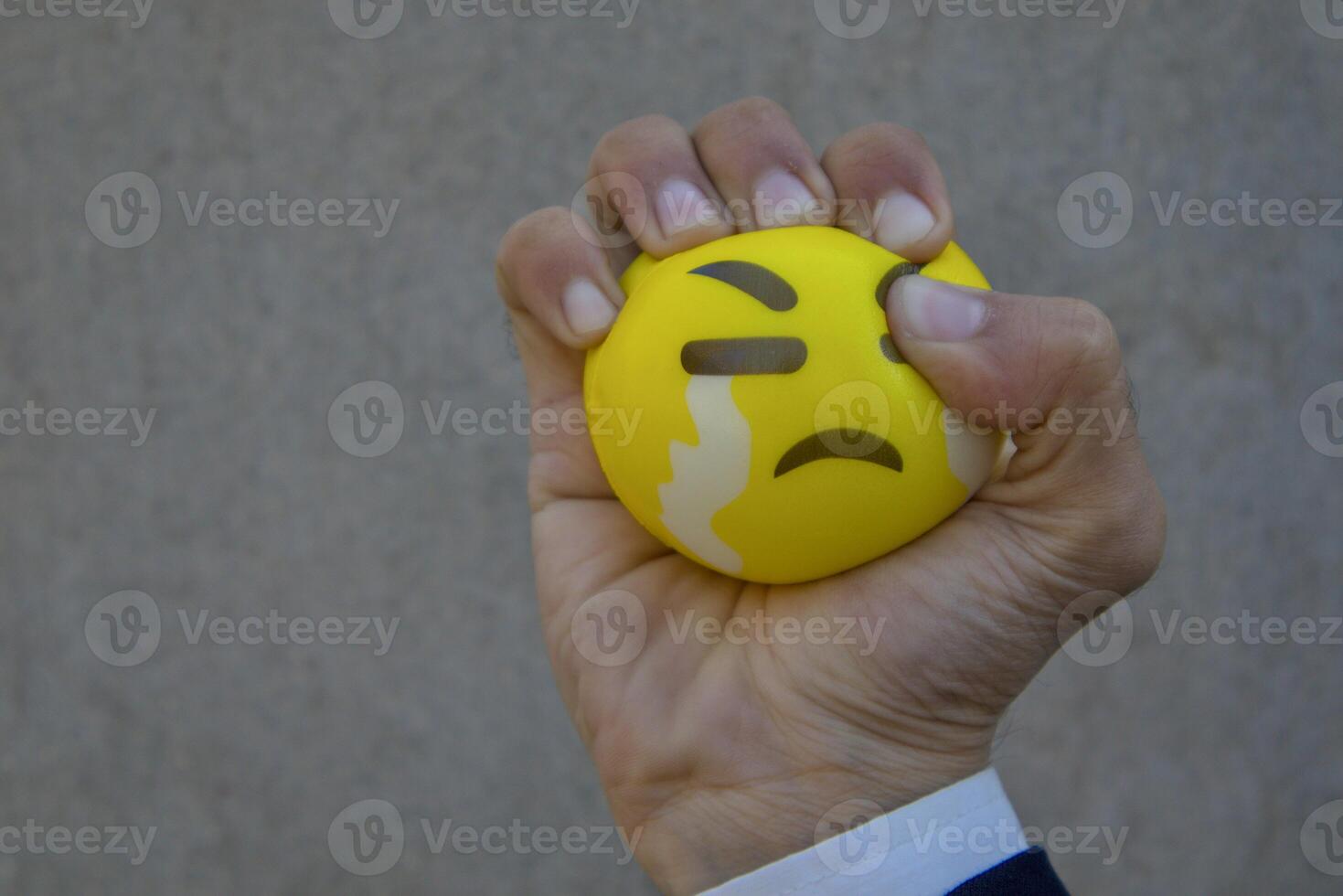 Hand Squeezing a Yellow Stress Ball with Crying Emoji photo