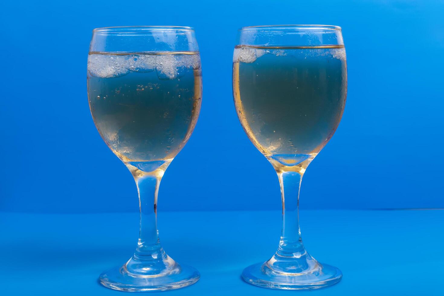 Close-up of two glasses of white wine with ice on a vibrant blue background photo