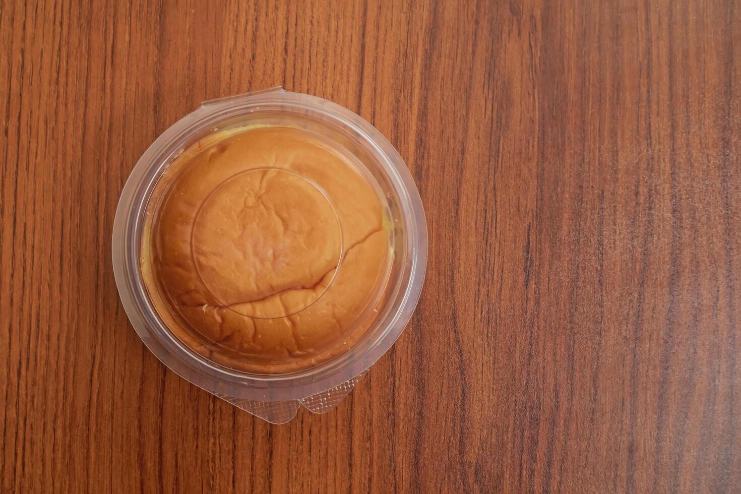Round butter bun in plastic packaging on a wooden table surface, top view photo