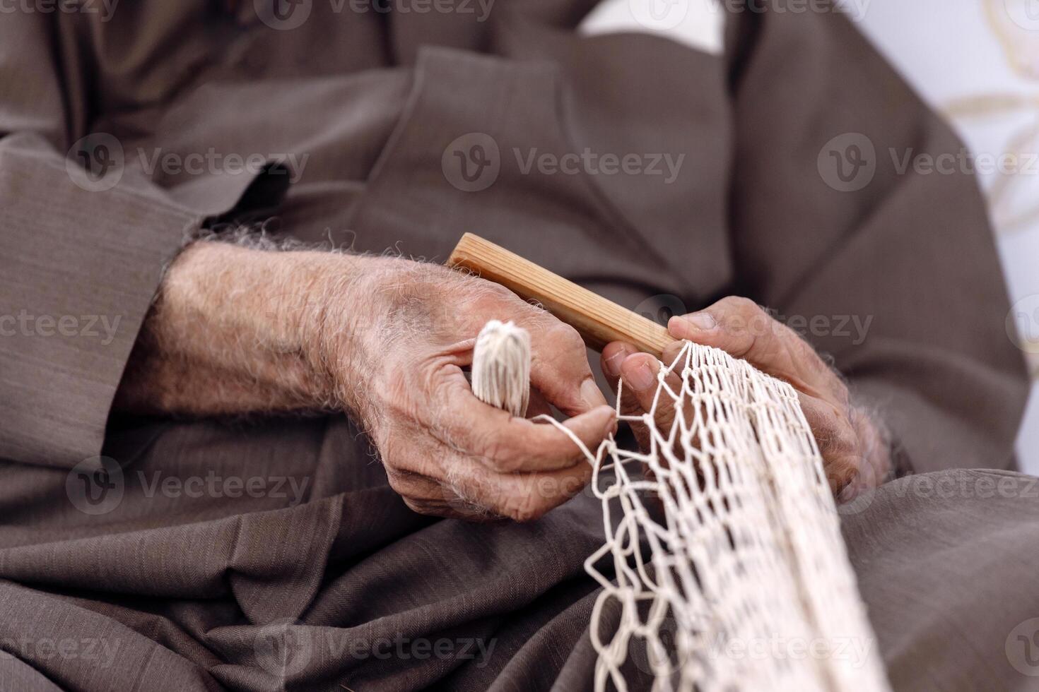 An old man is knitting traditional fishing net, hands in frame photo