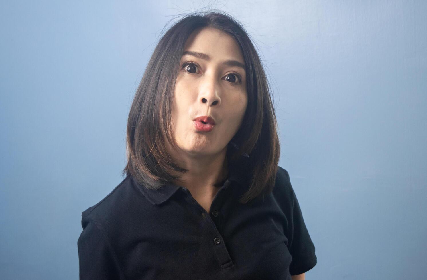 Asian woman wearing shirt black standing isolated blue background shocked face and wow surprise of impressed expression looking at camera photo