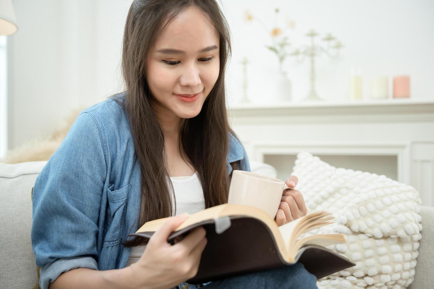 Young Asian woman enjoying reading book in living room at home photo