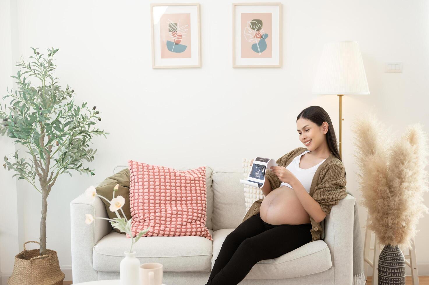 Pregnant woman holding ultrasound picture in living room at home photo