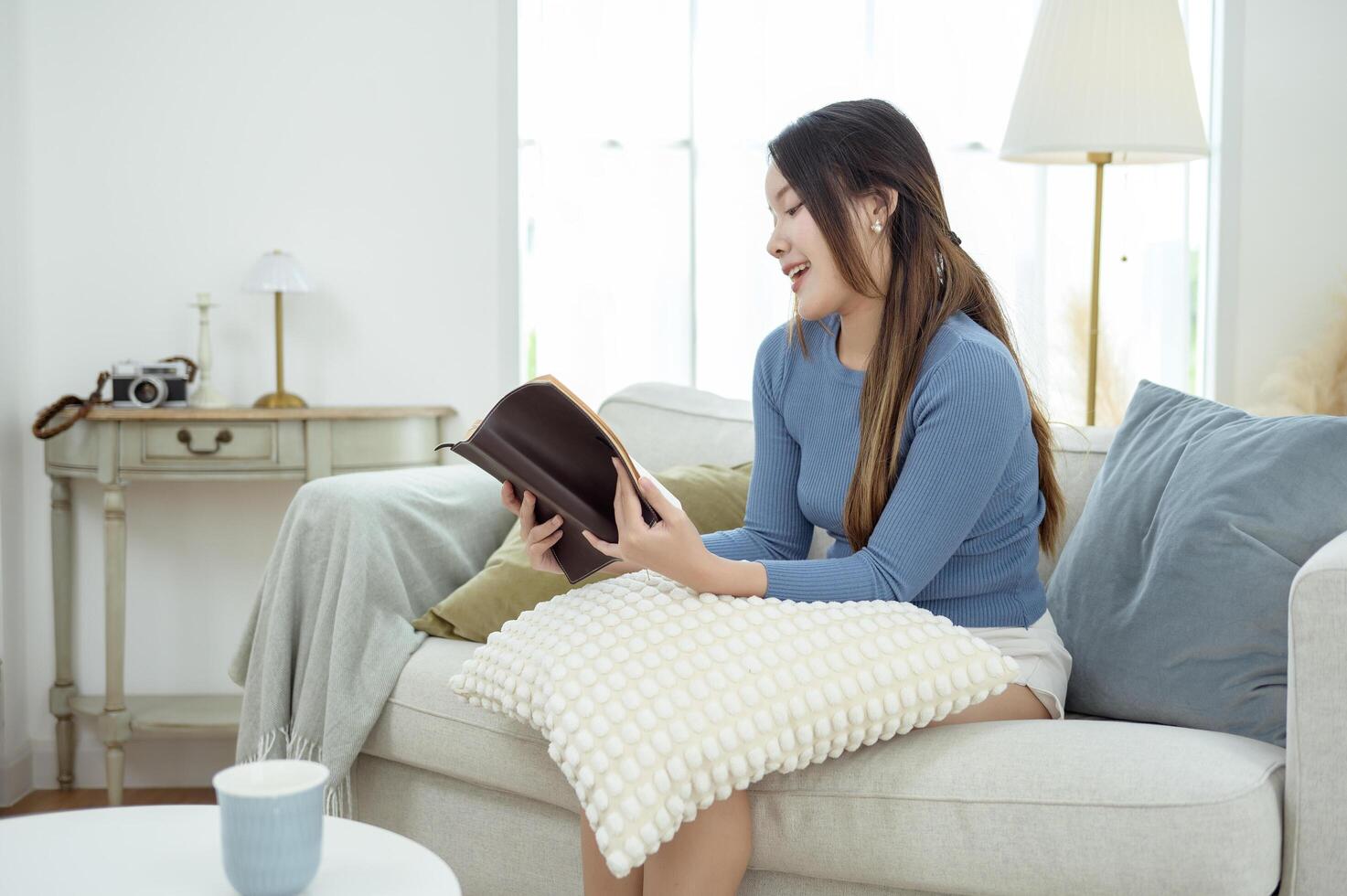 Young Asian woman enjoying reading book in living room at home photo