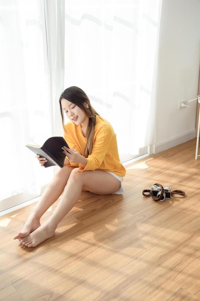 Young Asian woman enjoying reading book in living room at home photo