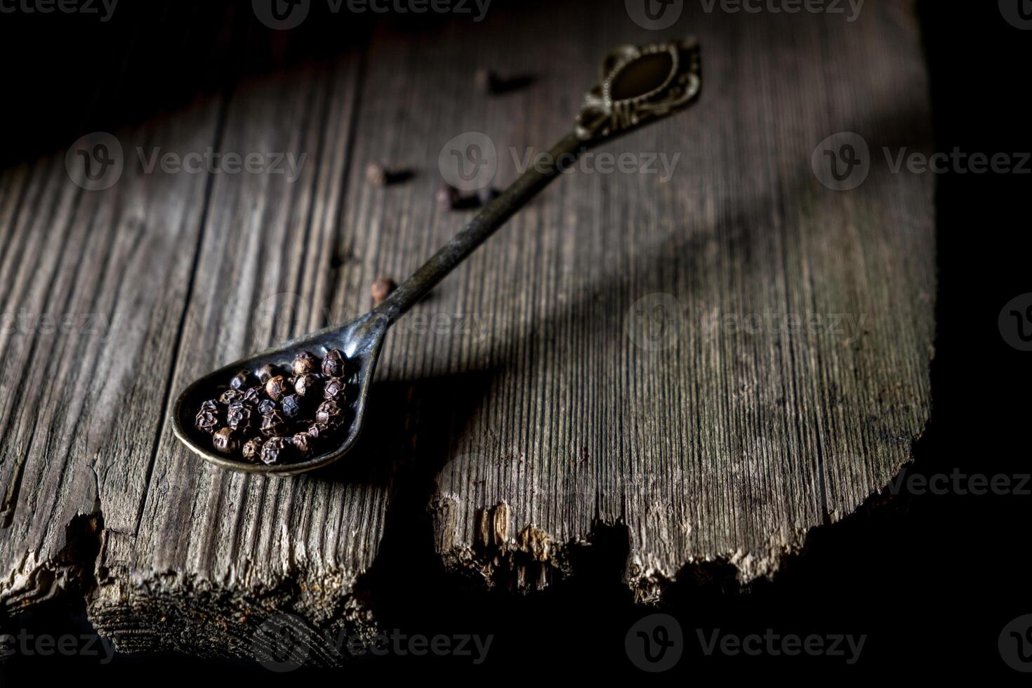 Vintage spoon with black peppercorns on rustic wooden surface, dark moody atmosphere, culinary ingredient concept, spice photography, natural textures, old wooden back. photo